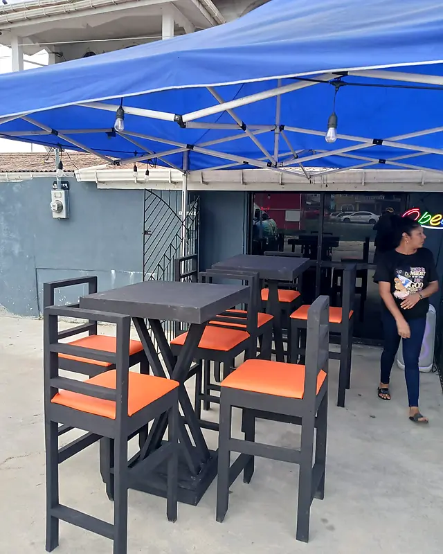 Black bar tables with orange-seat bar chairs set up under a canopy at a bar – Lynn's Furniture