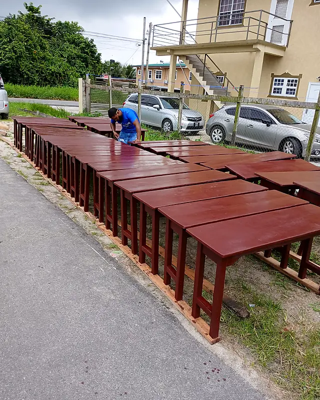Craftsman finishing two long rows of mahogany tables – Lynn's Furniture