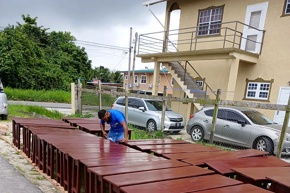 Craftsman finishing two long rows of new mahogany tables – Lynn's Furniture